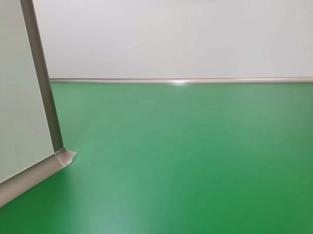 厂房车间环氧地坪施工实拍——环氧自流平,室内洁净空间,绿色环氧自流平地坪平整反光,墙面为白色金属边饰