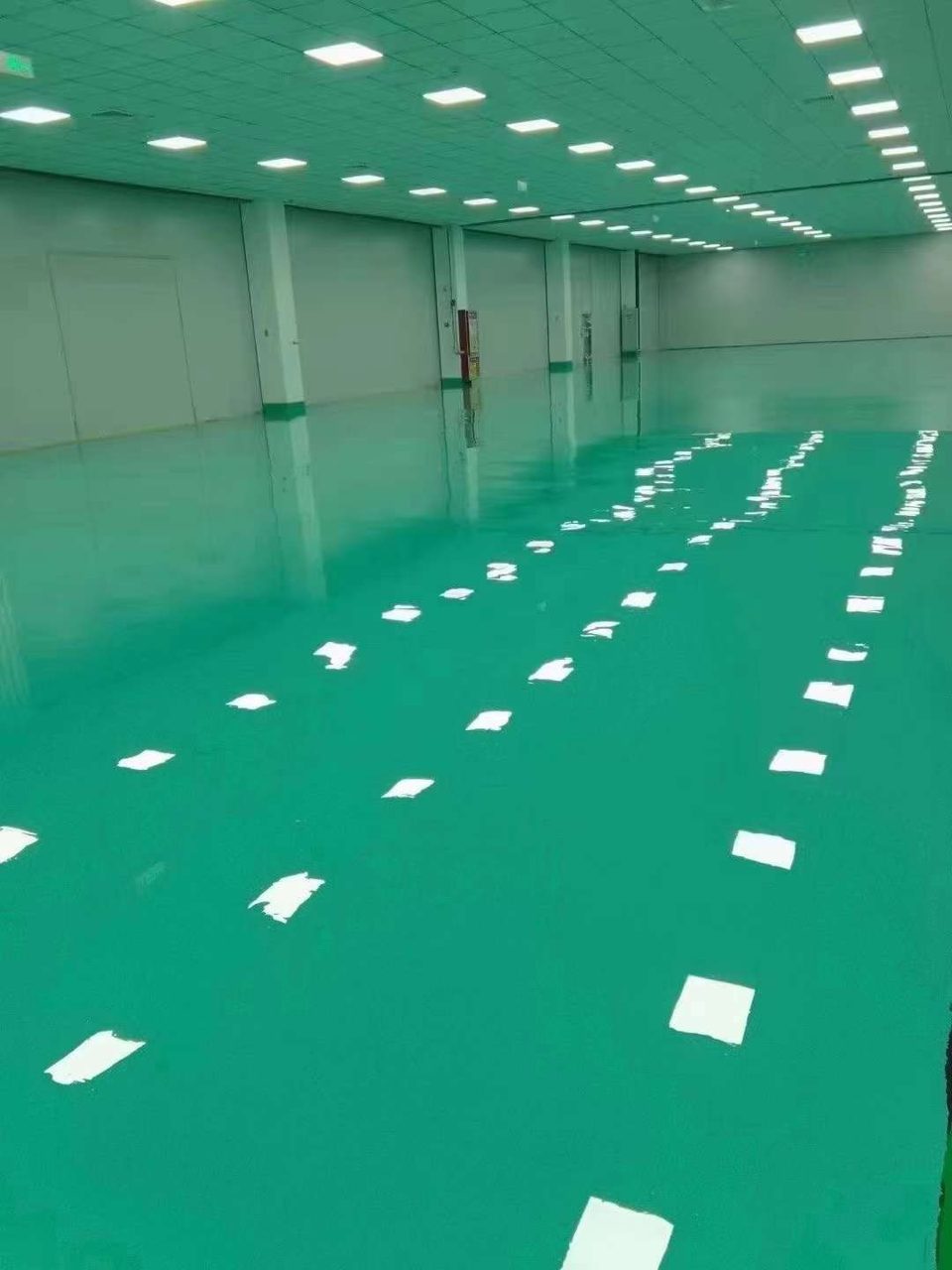 厂房车间环氧地坪施工实拍——环氧自流平,大开间厂房内完成的绿色镜面环氧自流平地坪,天花板照明灯光在地面形成清晰倒影