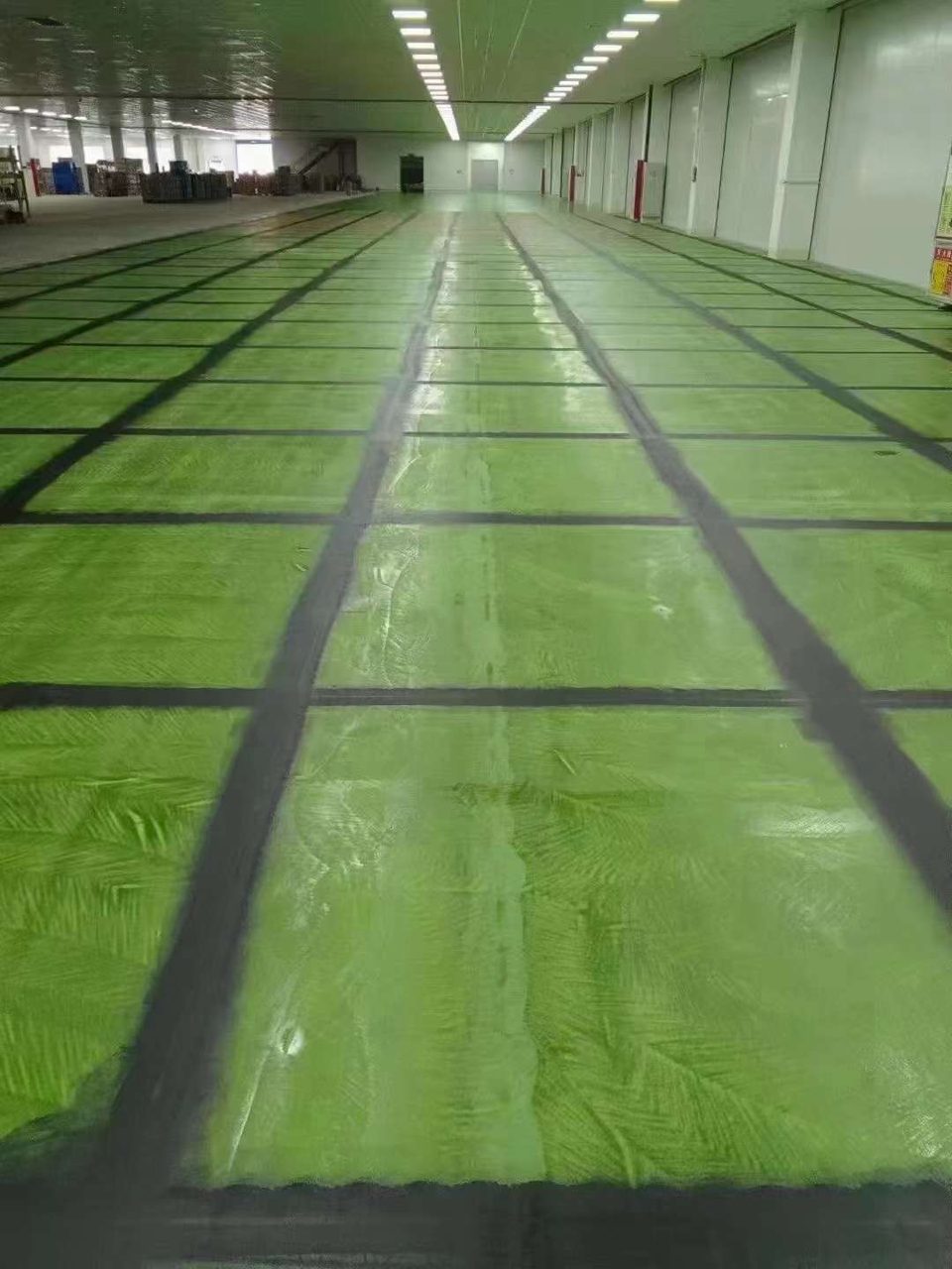 厂房车间环氧地坪施工实拍——环氧自流平,大开间厂房车间内的绿色环氧地坪,黑色分格线清晰,空间开阔