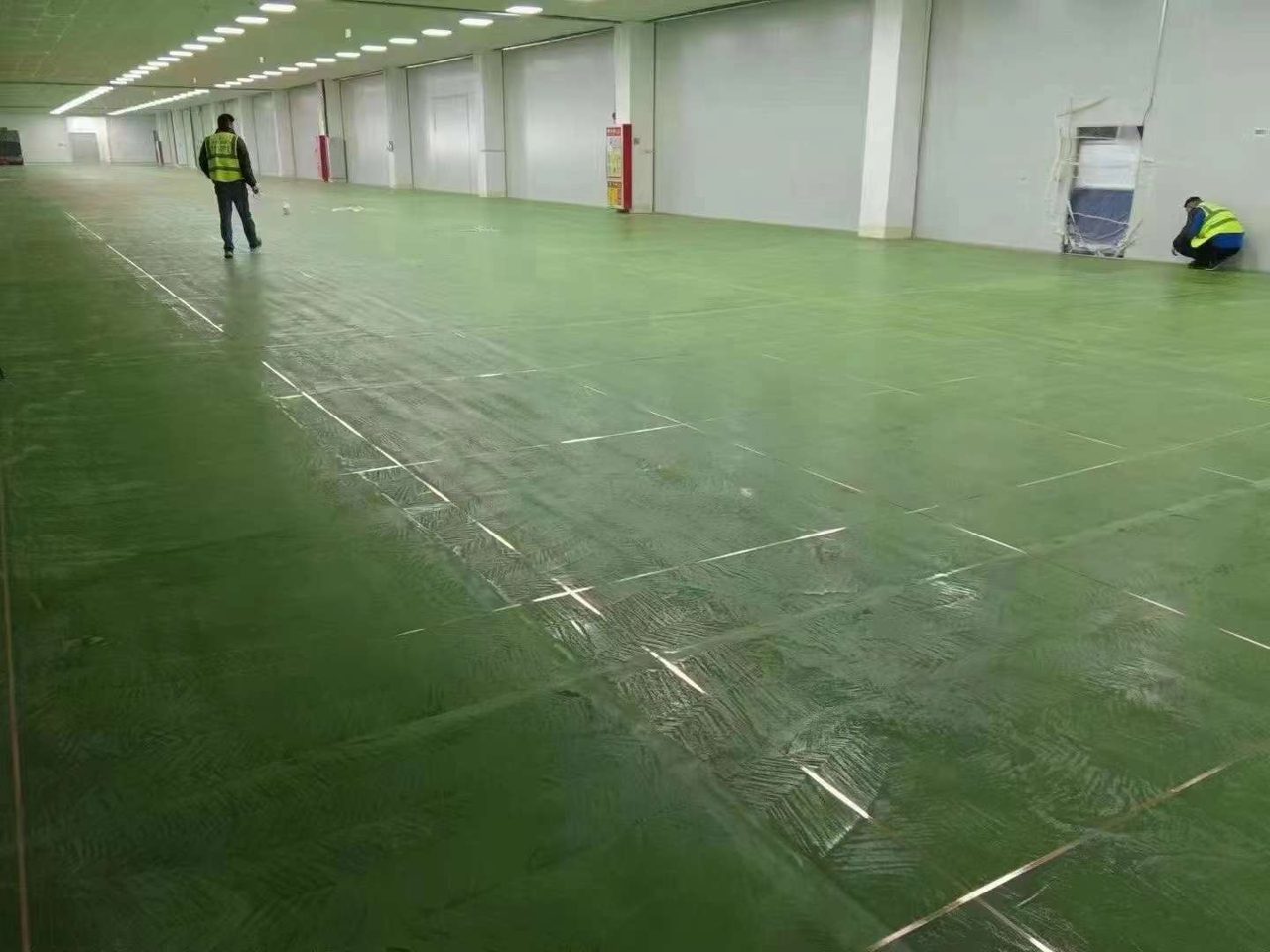厂房车间环氧地坪施工实拍——环氧自流平,厂房车间内正在施工的绿色环氧地坪,工人作业中,地面有分格线