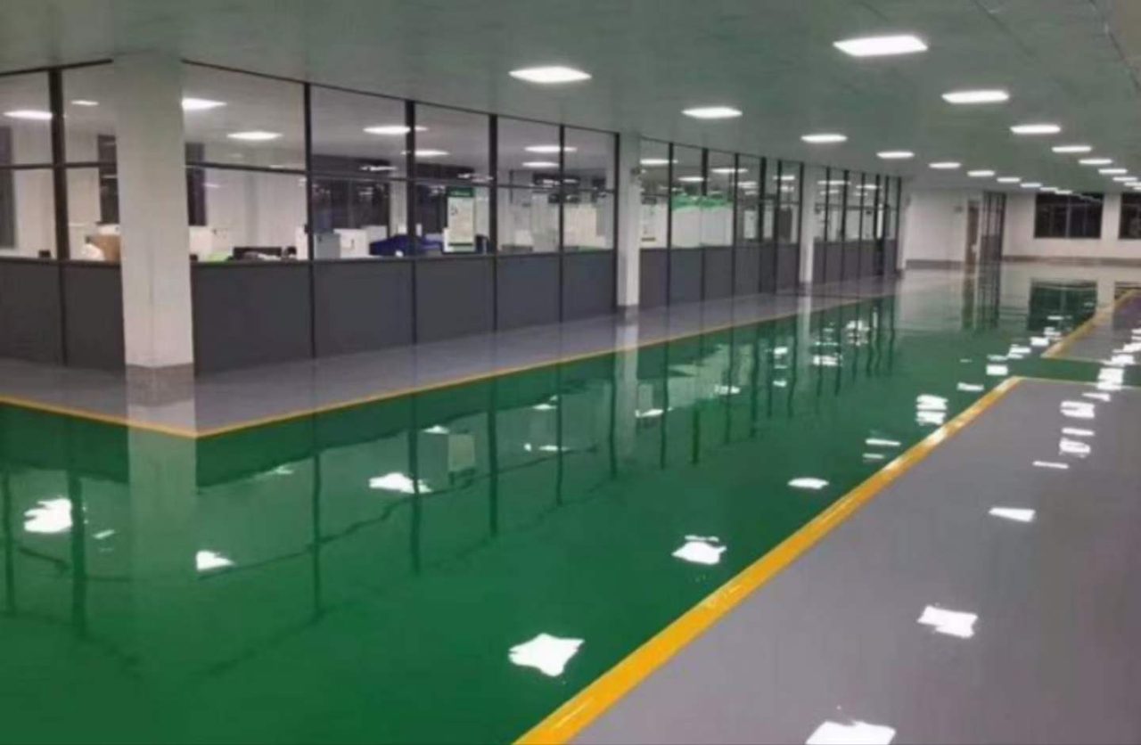 厂房车间环氧地坪施工实拍——环氧自流平,厂房车间区域环氧自流平地坪,镜面反光,一侧有玻璃隔间办公区,地面划分有绿色作业区