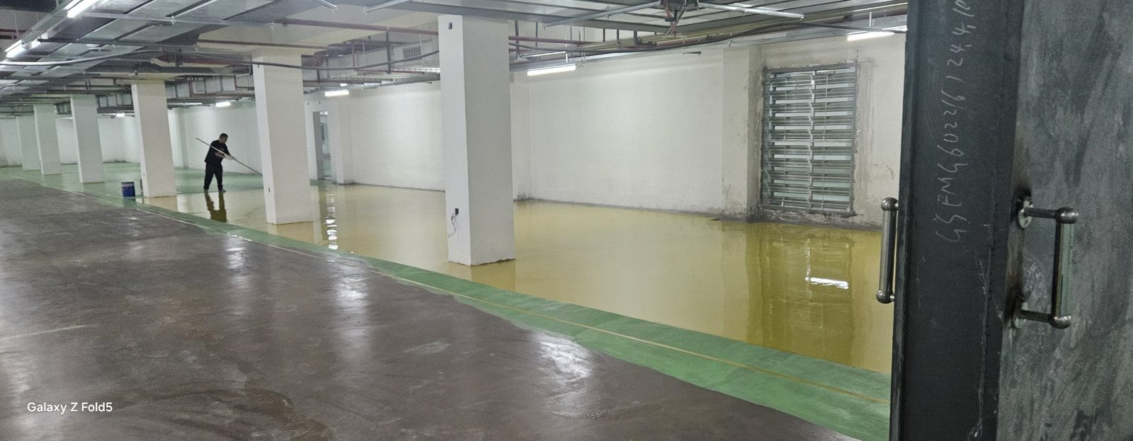 地下车库环氧地坪施工中：工人滚涂鹅黄停车位区域