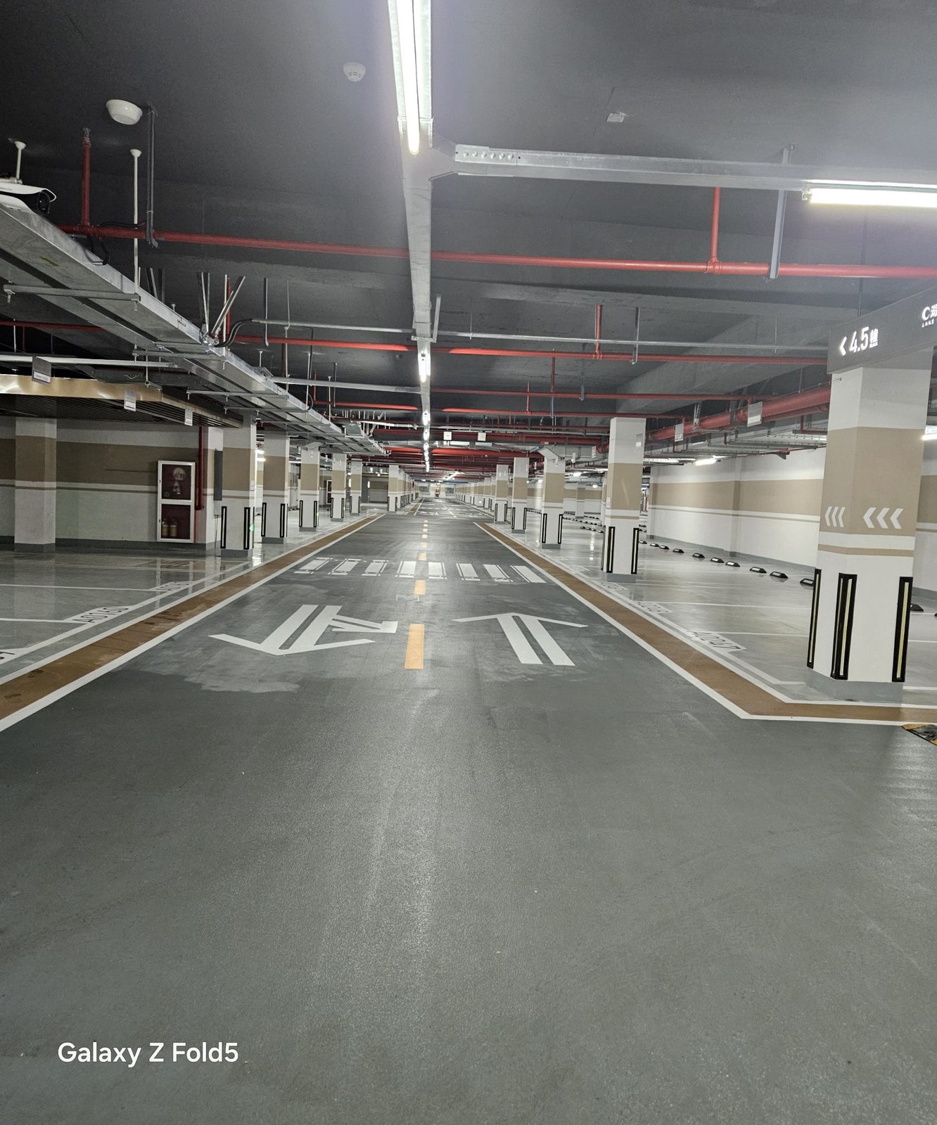 蓝城·云晟府地下车库：主行车道全景，深灰环氧地坪分向箭头与斑马线