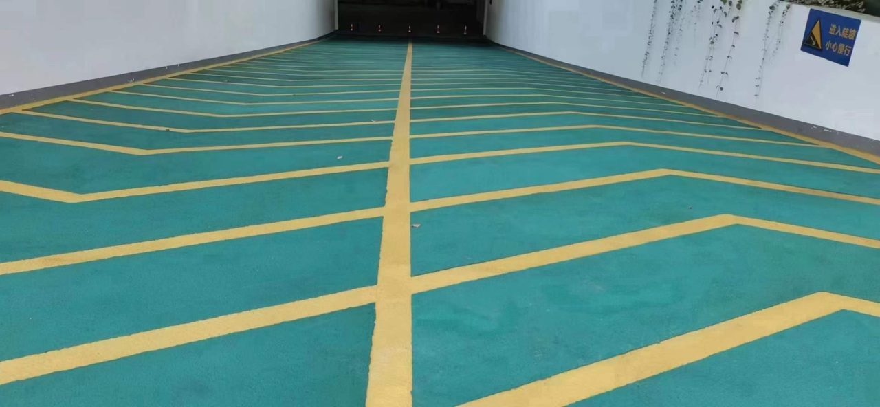 地下车库环氧地坪施工实拍——环氧砂浆，这是一处地下车库坡道，绿色防滑地坪配黄色标线，墙面设有交通警示标识