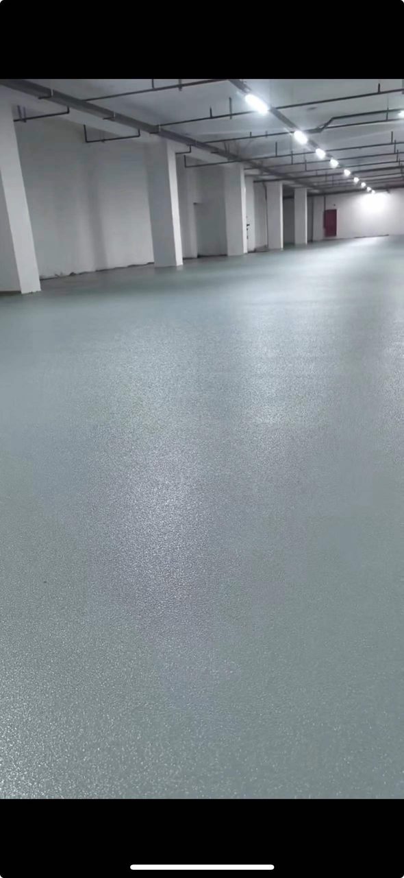 地下车库环氧地坪施工实拍——环氧砂浆，空旷的地下车库内场，地面呈均匀颗粒纹理，顶部为裸露管道与照明设施