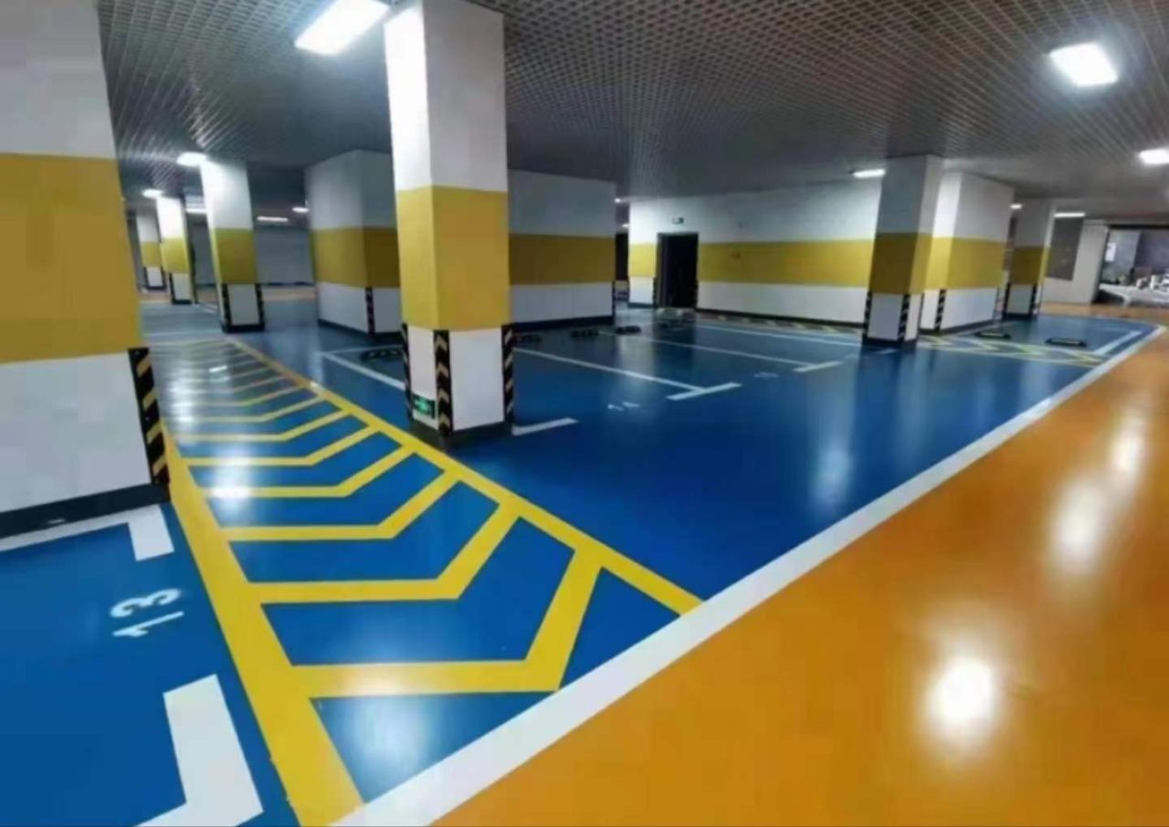 地下车库环氧地坪施工实拍——环氧自流平，该画面为地下车库施工后场景，地面为蓝色环氧自流平，可见车位线、柱体防撞条等要素