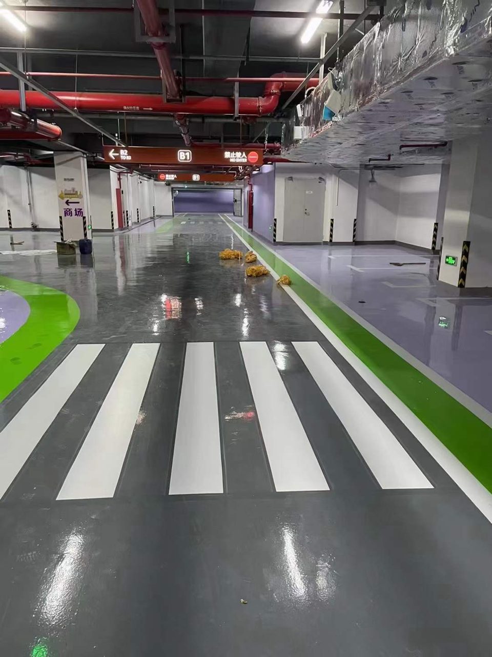 地下车库环氧地坪施工实拍——环氧自流平，该画面为地下车库施工后场景，地面为环氧自流平，可见行车道、斑马线、柱体防撞条等要