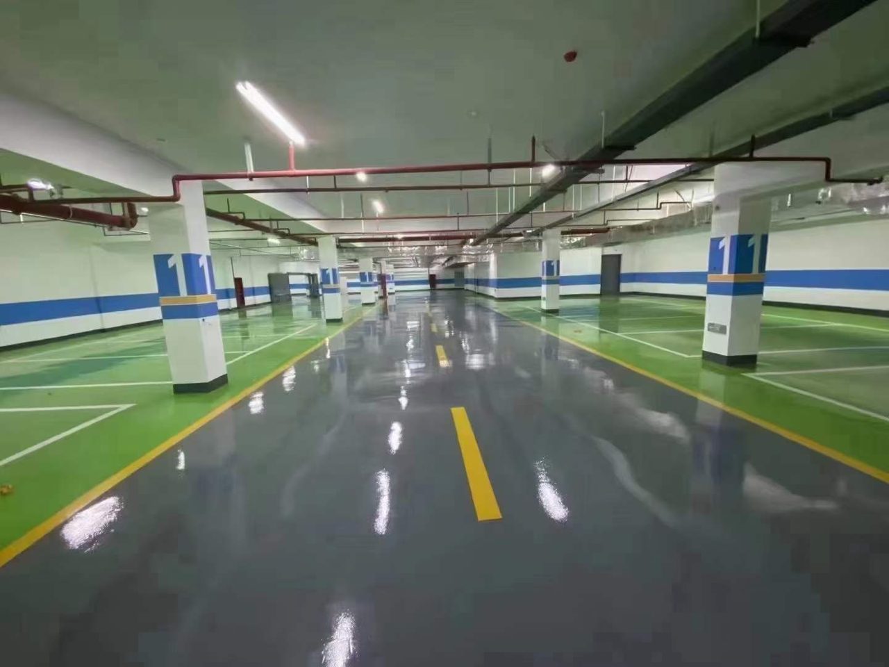 地下车库环氧地坪施工实拍——环氧自流平，地下车库环氧地坪施工完成，地面镜面反光，有清晰车位线与行车道分隔线