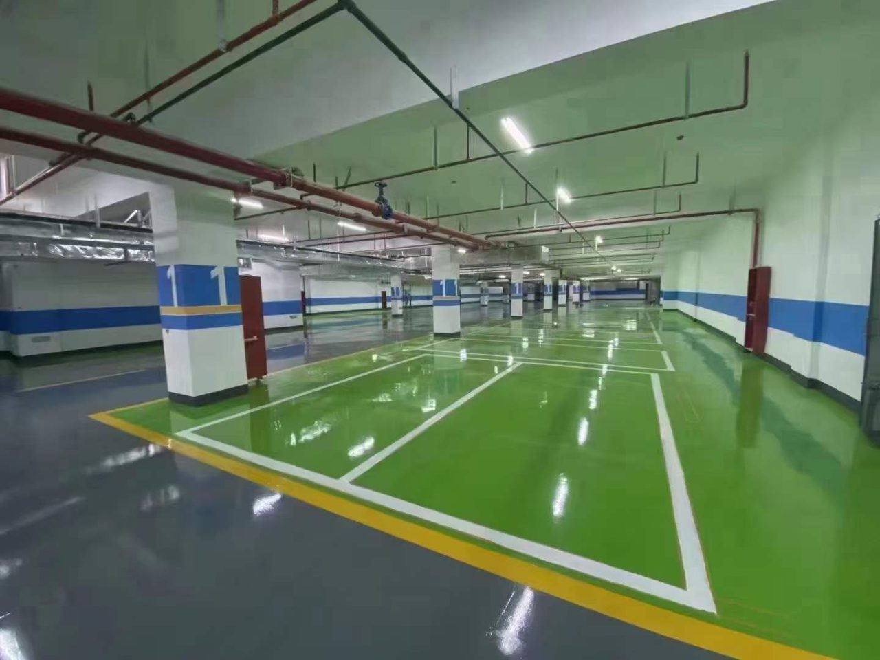 地下车库环氧地坪施工实拍——环氧自流平，地下车库环氧地坪施工完成，地面镜面反光，车位线清晰，柱体带有蓝色标识