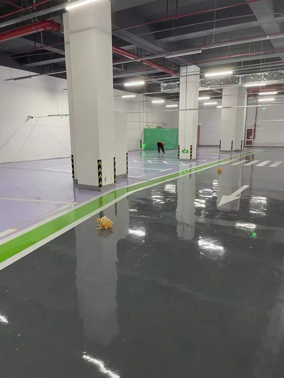 地下车库环氧地坪施工实拍——环氧自流平，地下车库环氧自流平地坪施工场景，地面镜面反光，可见车位线与柱体防撞条