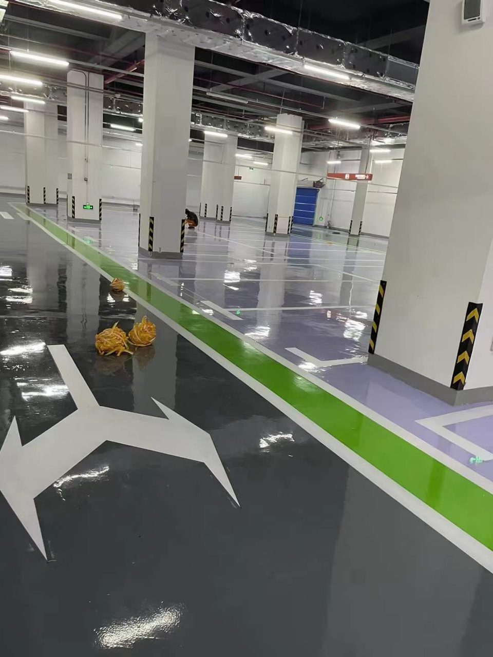 地下车库环氧地坪施工实拍——环氧自流平，地下车库环氧自流平地坪施工场景，地面镜面反光，可见行车指示箭头与柱体防撞条